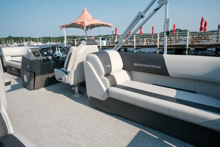 Interior of a pontoon boat with gray seats near a dock.