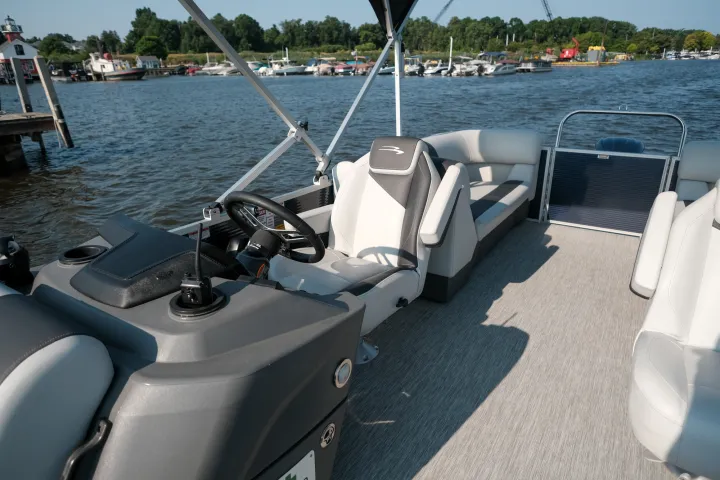 Pontoon boat interior with seating and steering wheel on a sunny day near a dock.