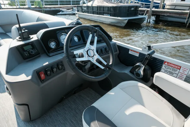 Steering wheel and dashboard of a boat docked by the water.