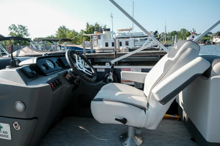 Boat interior with steering wheel and white captain's chair in a marina.