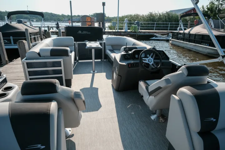 Interior of a pontoon boat with seating and a steering console by the dock.