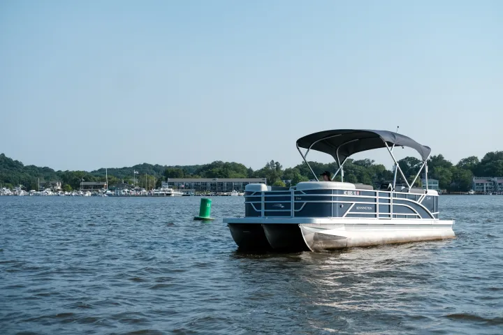 Pontoon boat on a lake with trees and buildings in the background.
