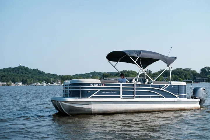 Pontoon boat on a lake with a person onboard under a canopy.