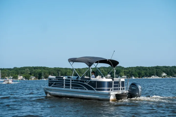 A pontoon boat with canopy cruising on a lake under clear skies.