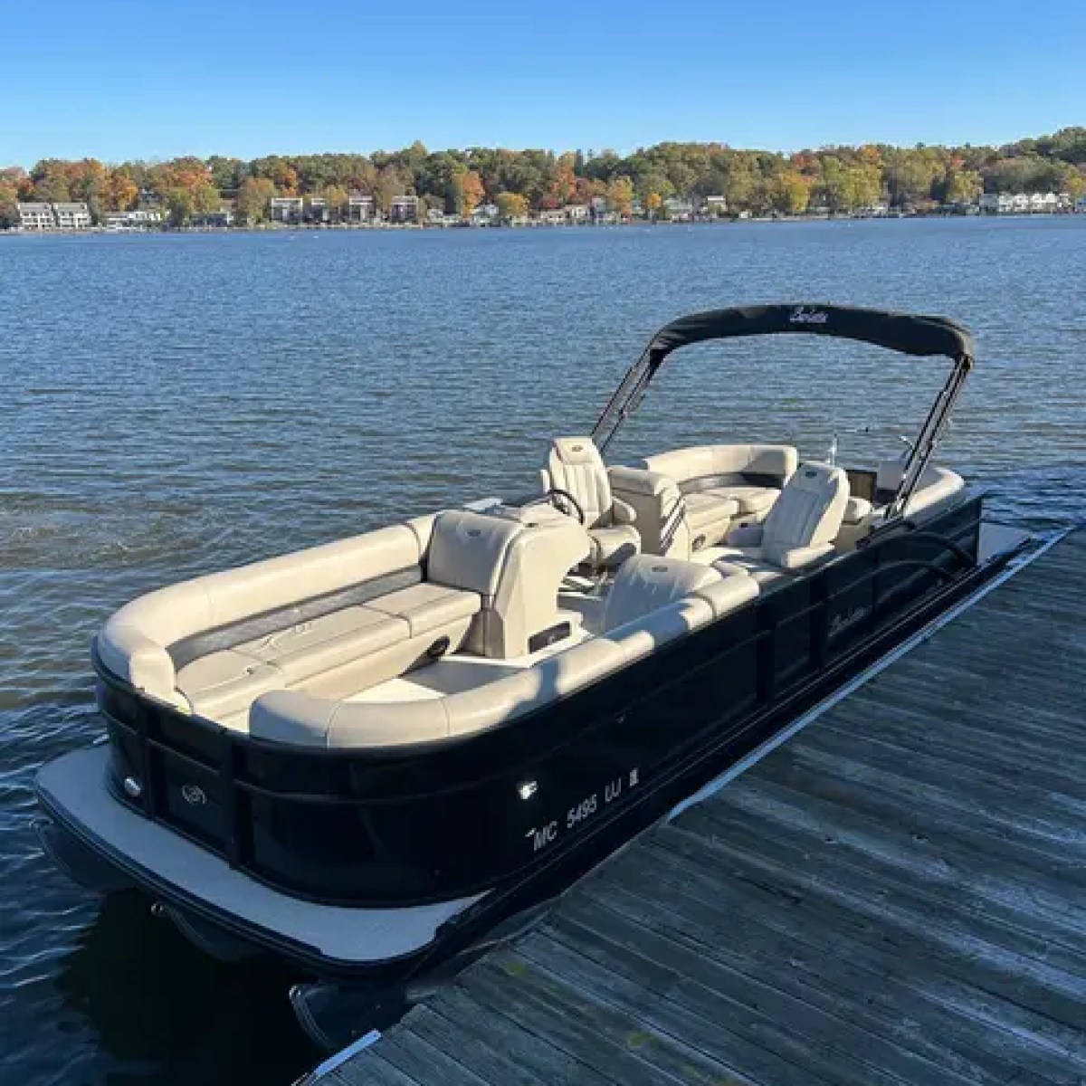 Pontoon boat docked on a lake with autumn trees in the background.