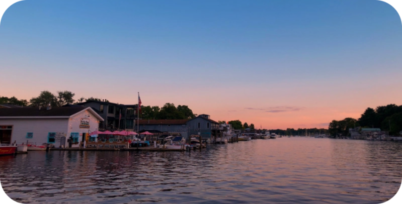 Sunset over a riverside with buildings and boats docked.